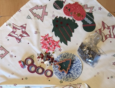 Ausgeschnittene Tannenbäume, Sterne, Weihnachtsbaumkugeln und anderes Baselmaterial auf dem Tisch